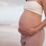 a serene image of a pregnant woman cradling her belly on a tranquil beach, symbolizing motherhood.