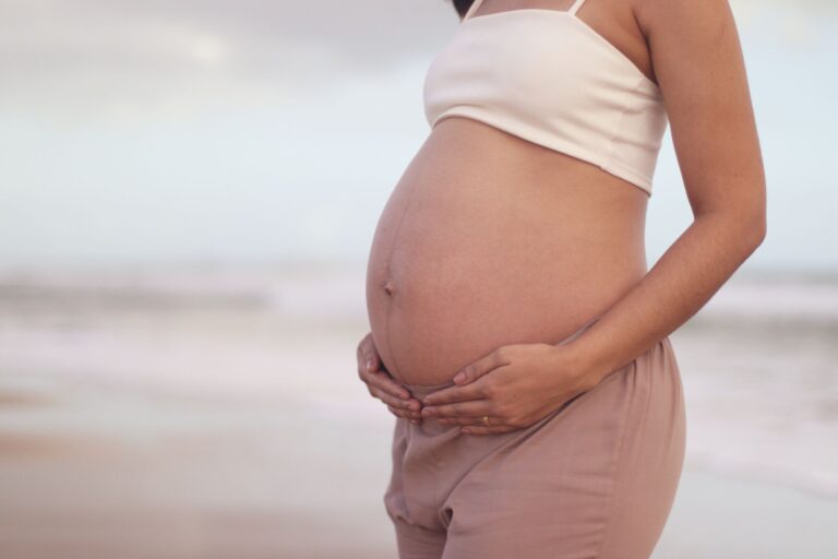 a serene image of a pregnant woman cradling her belly on a tranquil beach, symbolizing motherhood.