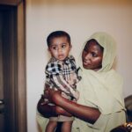 a mother lovingly holds her baby while indoors, showcasing their cultural attire.