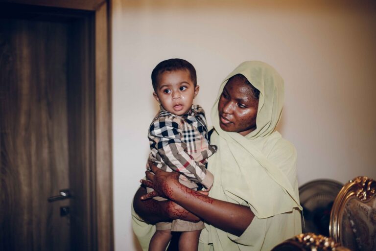 a mother lovingly holds her baby while indoors, showcasing their cultural attire.