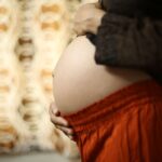 close-up of a pregnant woman gently holding her belly at home, symbolizing motherhood.