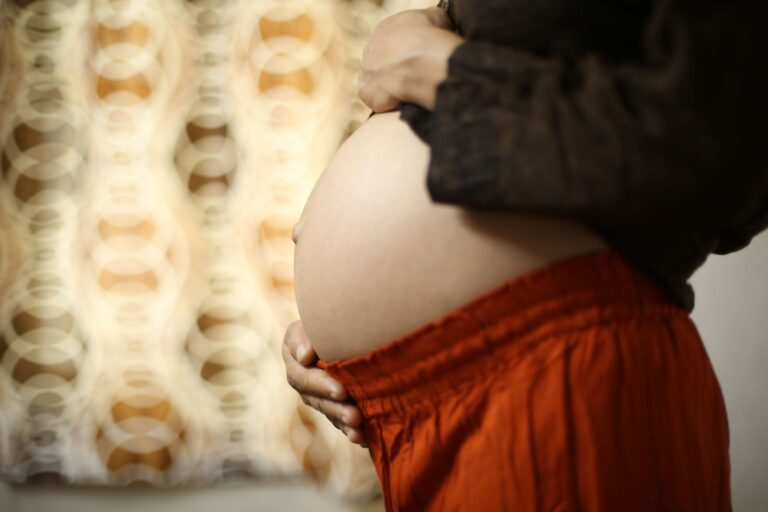 close-up of a pregnant woman gently holding her belly at home, symbolizing motherhood.
