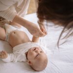 mother gently changes baby's onesie in a cozy home setting, nurturing and caring bond.