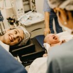 a mother smiles lovingly at her newborn in a hospital delivery room, attended by medical staff.