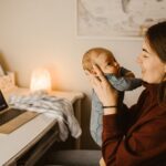 mother holding baby while video calling from home office. cozy and heartwarming indoor scene.