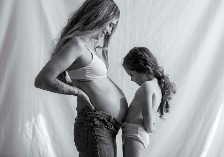 a heartwarming black and white image of a pregnant mother and her child sharing a tender moment indoors.