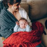 a tender moment of a mother holding her sleeping baby wrapped in a warm blanket indoors.