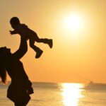 silhouette of a mother lifting her child at a sunset beach, capturing warmth and love.