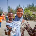 a joyful mother holding her baby in keffi, nigeria under a bright blue sky.