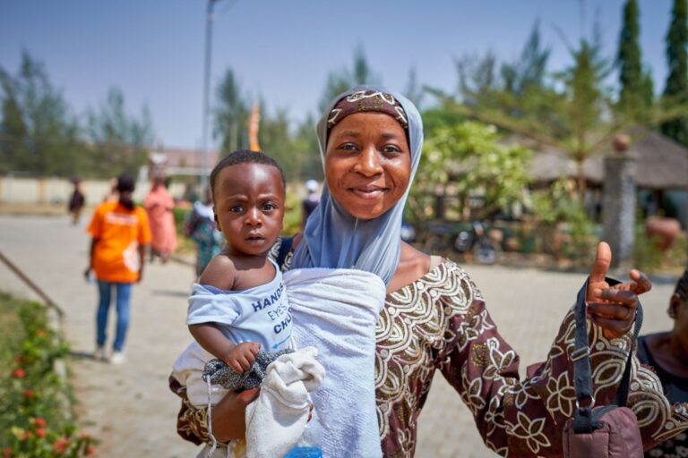 a joyful mother holding her baby in keffi, nigeria under a bright blue sky.
