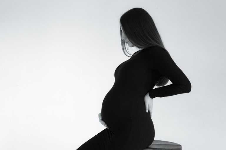 monochrome side view portrait of a pregnant woman sitting on a stool, embracing baby bump.