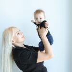 a happy mother lifts her baby in a bright, minimalist indoor setting.
