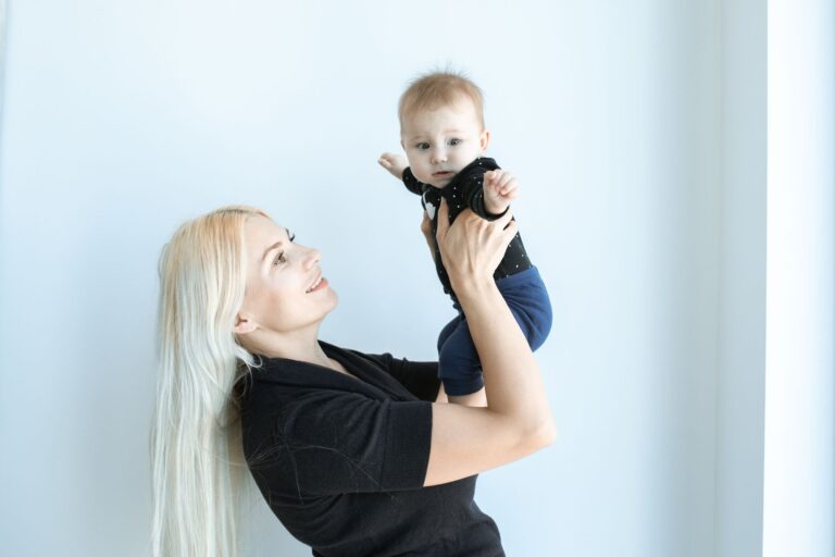 a happy mother lifts her baby in a bright, minimalist indoor setting.