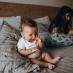 adorable baby plays happily on a cozy bed while mother relaxes nearby, creating a warm family moment.