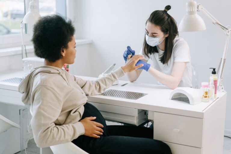 pregnant woman at a nail salon receiving a manicure from a nail technician.