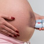 a pregnant woman holds blue baby shoes near her belly, showcasing motherhood anticipation.