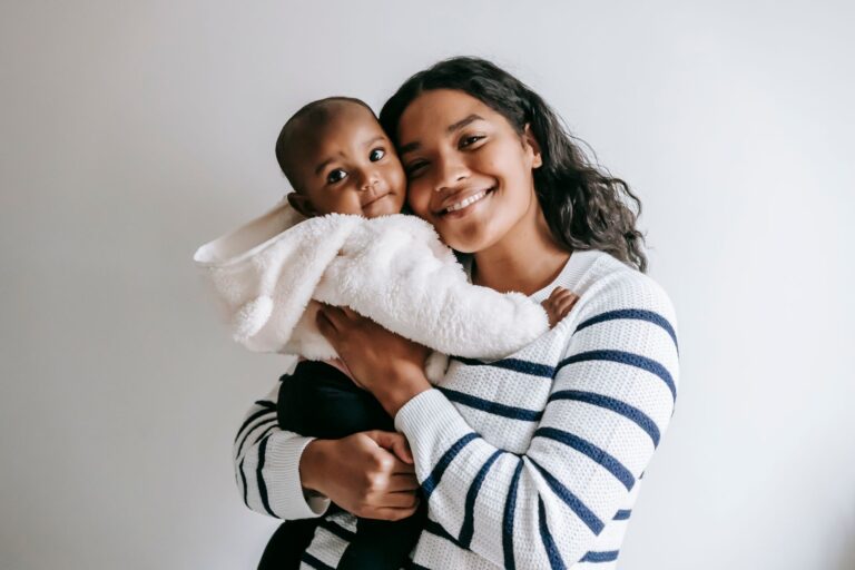delighted african american mother cuddling cute little black baby while smiling and looking at camera on white backgroun
