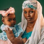 a mother lovingly holds her baby, both dressed in vibrant traditional nigerian attire.