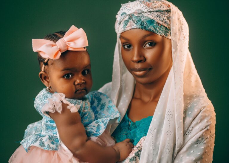 a mother lovingly holds her baby, both dressed in vibrant traditional nigerian attire.