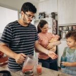 a family bonding moment in the kitchen as parents prepare juice for their children.