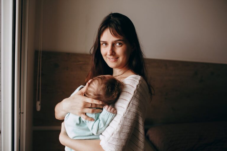 a mother lovingly holds her sleeping baby indoors by a window, capturing a warm and intimate moment.