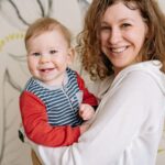 happy mother holding her smiling baby, both looking at the camera indoors.