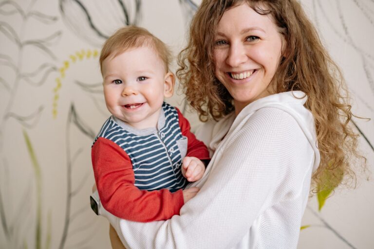 happy mother holding her smiling baby, both looking at the camera indoors.