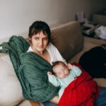 a mother lovingly holds her sleeping baby on a cozy sofa, surrounded by warm blankets.