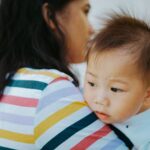 a woman lovingly holds an asian baby boy indoors, showcasing a tender family moment.