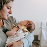 side view of crop caring mother in casual wear with cute newborn baby in arms standing in light room at home