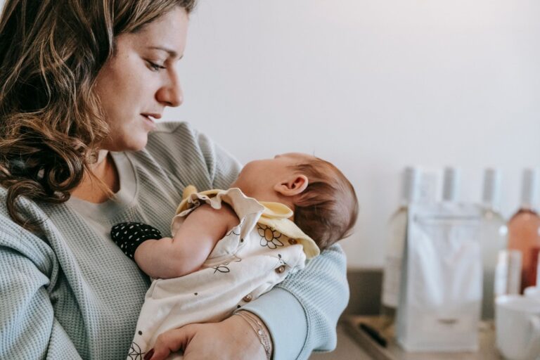 side view of crop caring mother in casual wear with cute newborn baby in arms standing in light room at home