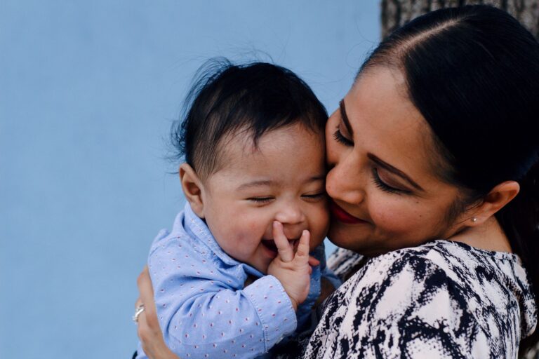 a mother affectionately embraces her baby against a serene blue background.