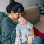 a mother lovingly holds her sleeping baby on a cozy sofa, wrapped in warmth and affection.