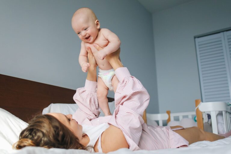 mother lifting her happy baby in a loving gesture on a bed in a cozy bedroom.