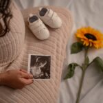 expectant mother holding an ultrasound with baby shoes and a sunflower, symbolizing new beginnings.