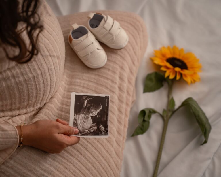 expectant mother holding an ultrasound with baby shoes and a sunflower, symbolizing new beginnings.