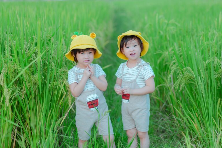 charming twin sisters in yellow hats enjoying a sunny day in a lush green field.