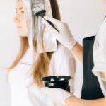 hairdresser applying color to woman's hair in salon using brush and foil technique.