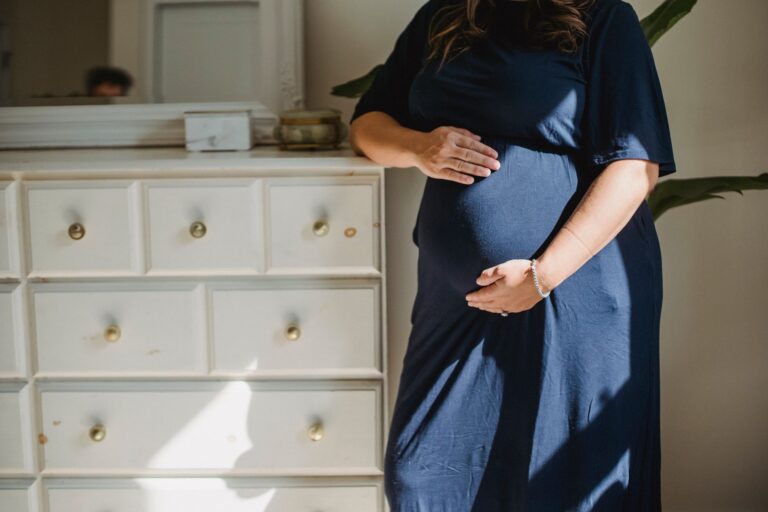 crop anonymous expectant female caressing gently belly near commode in house room in sunlight