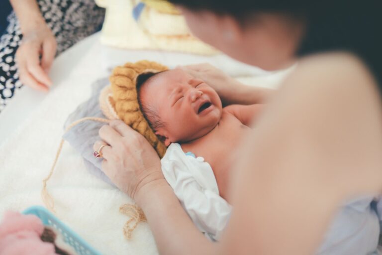 a crying newborn baby lying on a bed while being comforted by a parent, showcasing early life moments.