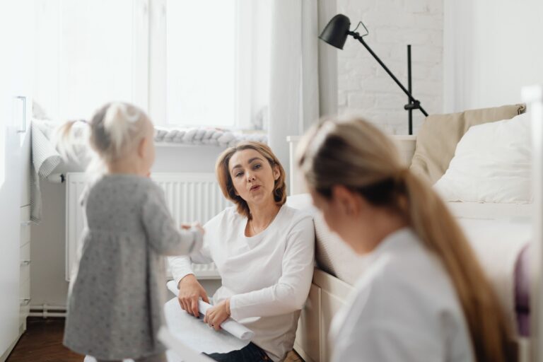 a mother sits on the floor talking with her daughter in a cozy bedroom setting.