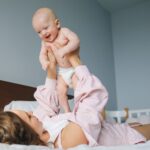mother lifting her happy baby in a loving gesture on a bed in a cozy bedroom.