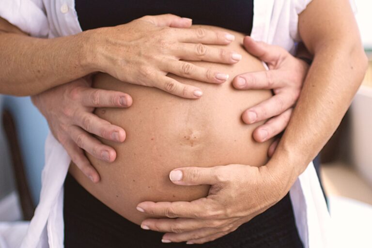 close-up of a couple's hands lovingly holding a pregnant belly, symbolizing family and expectation.