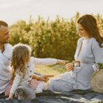 a family enjoys a picnic outdoors, celebrating a pregnancy announcement.