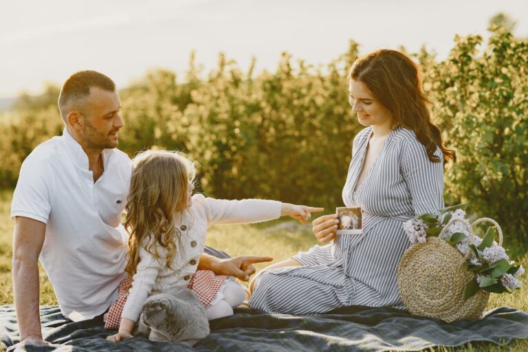a family enjoys a picnic outdoors, celebrating a pregnancy announcement.