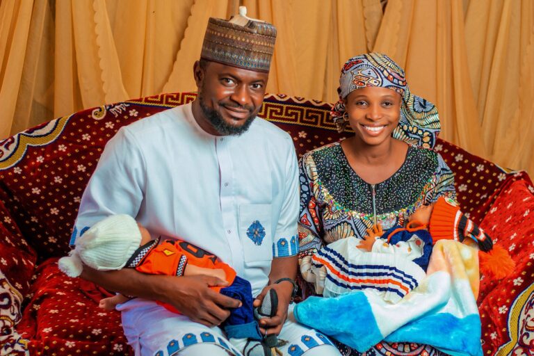 joyful african parents holding twins in traditional attire, vibrant setting.