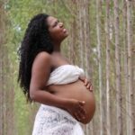 african american pregnant woman with curly hair standing in a serene forest setting.