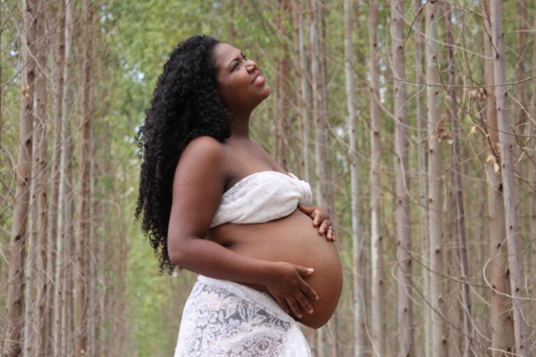 african american pregnant woman with curly hair standing in a serene forest setting.
