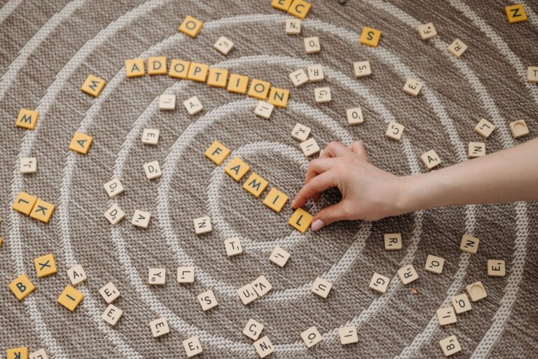a hand arranges letter tiles spelling 'family' and 'adoption' on a circular patterned carpet.