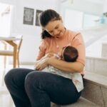 woman smiling and cradling baby on stairs indoors, portraying warmth and family bonding.